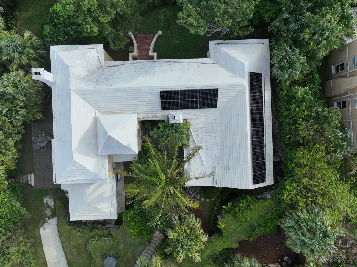 A Bermuda home among palms with solar panels on its white roof, seen from directly above